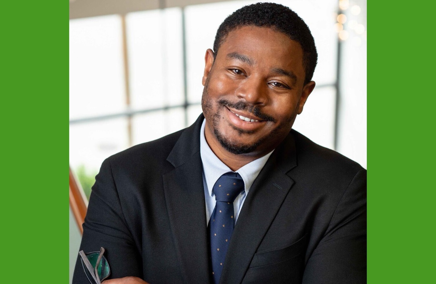 Ali Knight newsmaker headshot: black man in suit smiling while leaning to his left in front of bright background