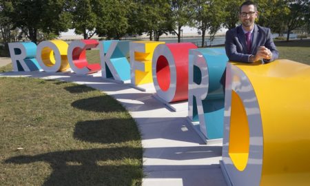 cities and youth in violence: mayor in suit poses next to Rockford sign