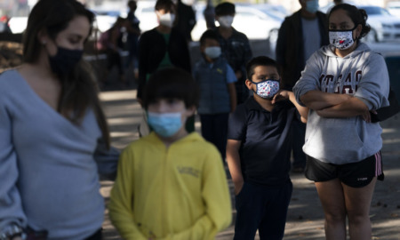 Afterschool funding: Parents & children wearing masks standing in line outside.