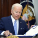 gun safety bill: President Biden, white-haired man in navy suit, white shirt and light blue tie, sidns page in large, open cook.