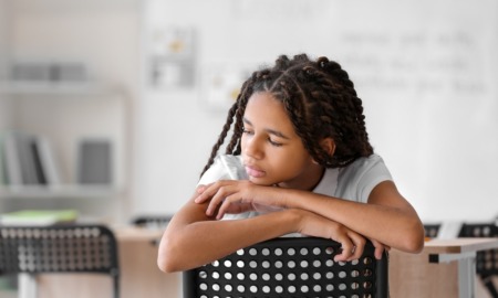 Black girls record rates of self-injury and suicide: young black girl sitting backwards in chair in classroom looking off to the side sadly