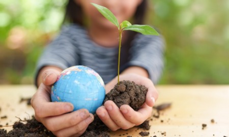 environmental project grants and education grants: little girl holding globe and newly sprouted tree in soil