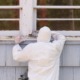 EPA proposes lower lead exposure limit in daycares, homes: person in hazmat suit painting the exterior window sill of older home