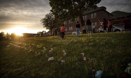 US church boarding school pasts: memorials of lights and flowers on grass in front of building and tree at sunset