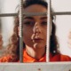 girls in juvenile justice support grants: young brunette girl in orange detention garb looking at camera from behind bars