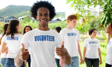 youth-led projects, youth-led community projects grants: happy young black man in volunteer shirt giving thumps up with other youth volunteers in background