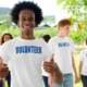 youth-led projects, youth-led community projects grants: happy young black man in volunteer shirt giving thumps up with other youth volunteers in background