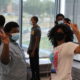 Afterschool programs use data to meaure outcomes: Eight masked teens stand in white room with large windows; two black girls in front flashing peace sign with hands