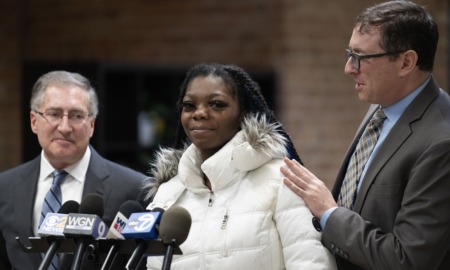 Lawsuit; Illinois agency wrongfully imprisoned children: young black woman in white coat talking into microphones with men in suits at her side