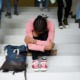 Mental health: young black girl sitting on school steps with head lowered and hugging her legs