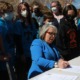 New Mexico offers equal pay to Native American teachers: older woman surrounded by people in matching blue Native logo shirts signing a document