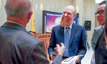 CYFD: Smiling man with red beard talks to other men in hallway, all wearing business suits.