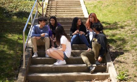 School start times: Six teen students sit on wide, long, outdoor, cement steps going up grassy hill.