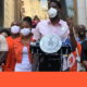 gun violence: Man in short-sleeved pink shirt, mask speaks at outdoor podium surrounded by crowd wearing masks