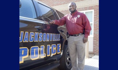 police: smiling man with red shirt, khaki pants leans on SUV labelled Jacksonville Police