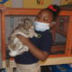 Atlanta school: Little girl wearing mask holds rabbit near cage. Partially seen adult stands to left of her.