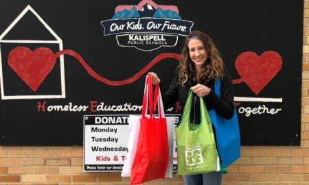 Montana: Smiling woman holds tote bags of different colors in front of sign on brick wall