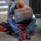 New York homeless payments: A homeless male sits on a New York City sidewalk holdwith head hanging hidden behind large cardboard sign with a message asking for help.