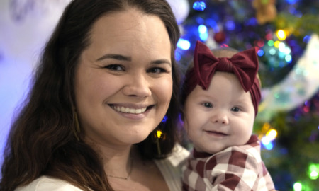 Abortion and Adoption: Close-up of smiling young dark-haired woman holding infant in red plaid top with large red bow headband.