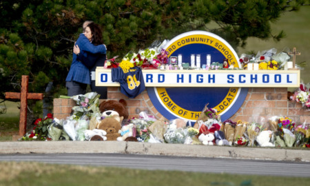 school shooting: Oxford high school sign covered in flowers and memorial items while two people hug