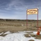 Native American Education: Tellow wood sign on two red poles with red letters reading "Warriors' Field" stands alone in a desert landscape.