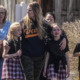 Gun violence: 3 adults , one woman hugging two of the three children, walk with crying children outside during the day.