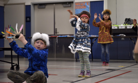 Native American afterschool programs: Several young children stand and sit in a classroom with vo desks