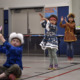 Native American afterschool programs: Several young children stand and sit in a classroom with vo desks