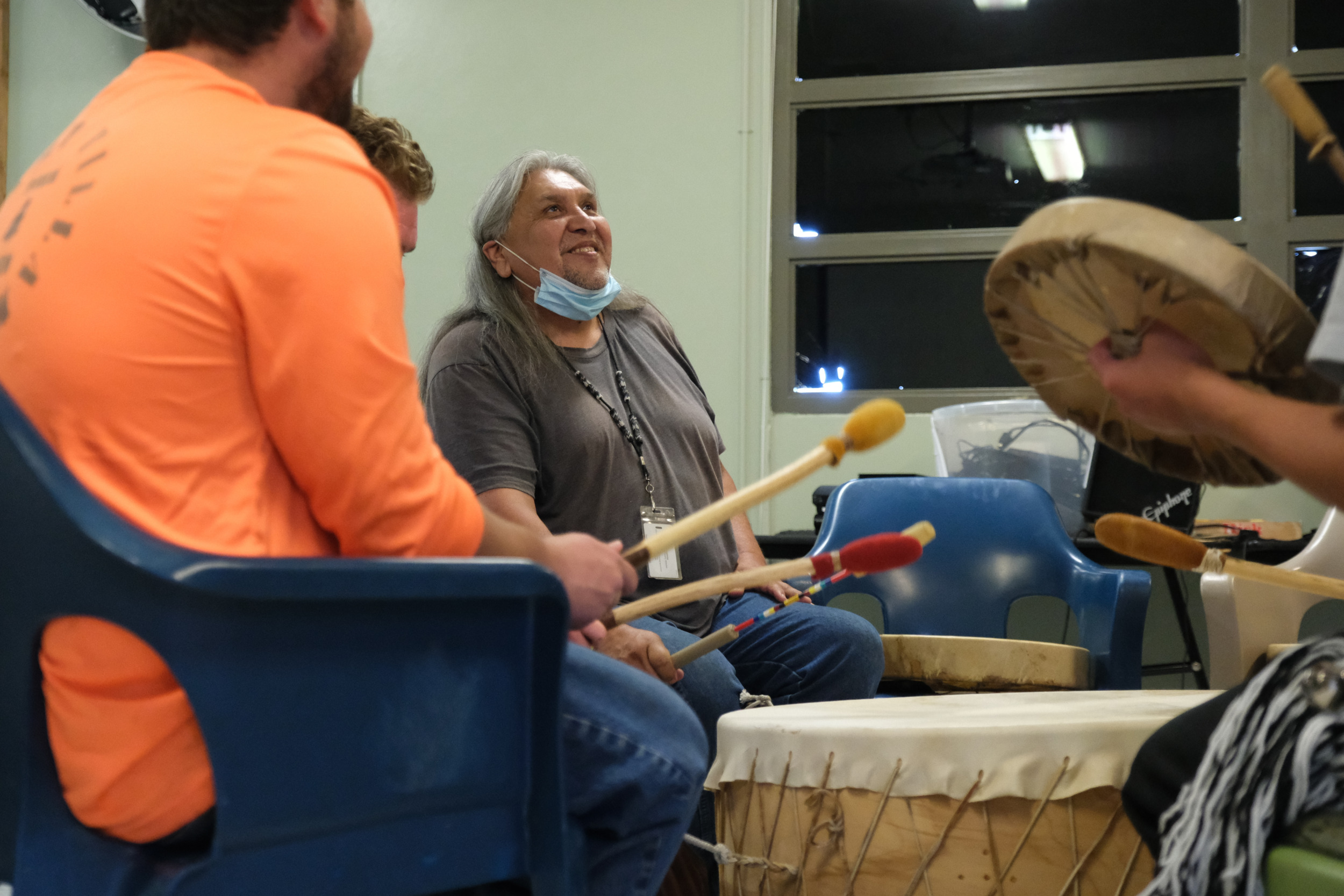 Native American rituals: Native American elder man with long gray hair sits on floor leading a drum circle