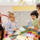 Califonia pre-kindergarten: Five young children sit at round table with two fenale teachers doing art activities