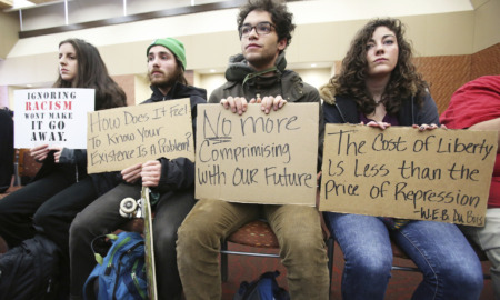 student free speech: 4 yoiung adults sit on a bench holding protest signs