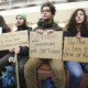 student free speech: 4 yoiung adults sit on a bench holding protest signs