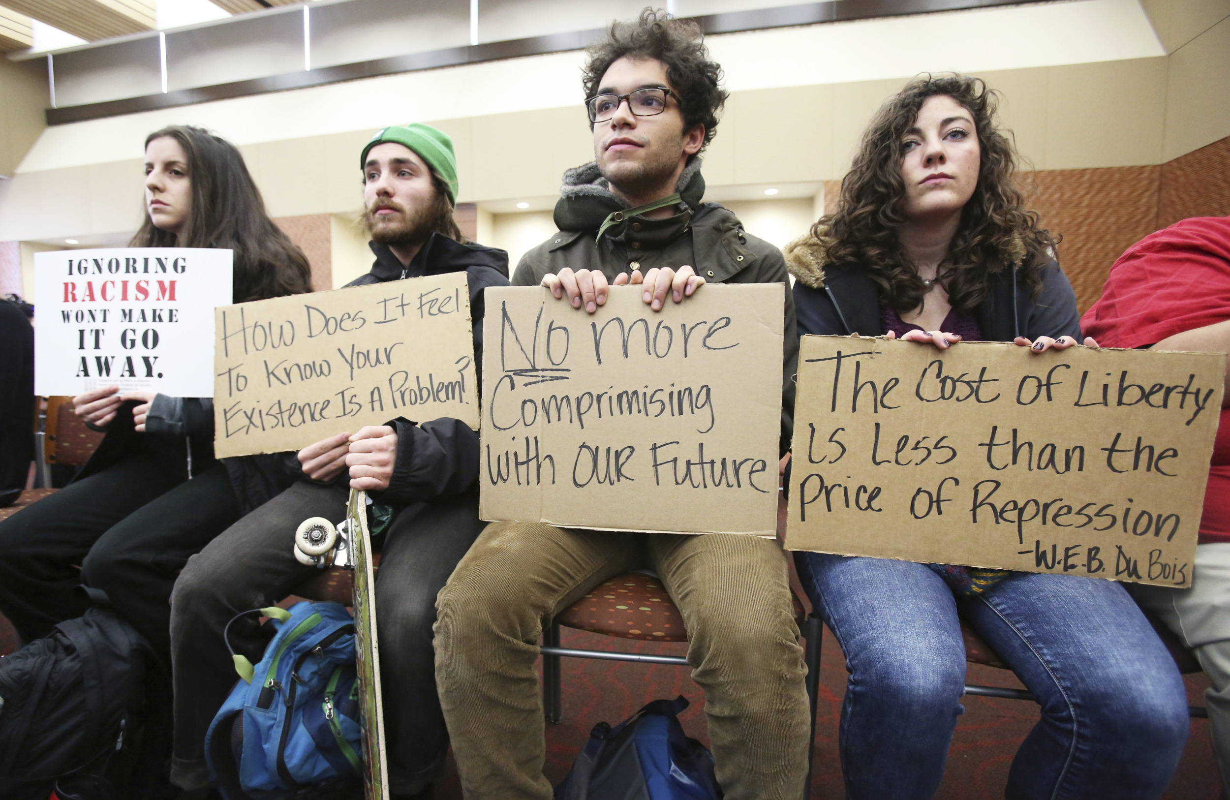 student free speech: 4 yoiung adults sit on a bench holding protest signs