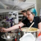 Disabled students' shorter school days: Teen girl with turquoise hair pulled back wearing black t-shirt reaches across several stainless steel mixing bowls for baking tools hanging on the wall in a commercial kitchen.