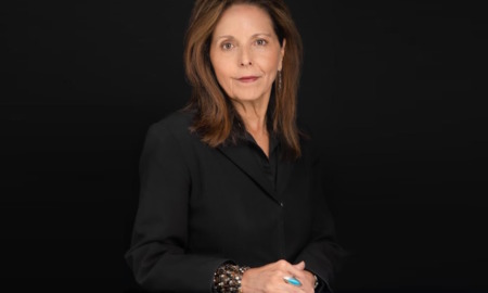 Juvenile justice reform: Katherine Lucero headshot woman with long, brown hair in black blouses sits with hands folded in front of black background