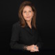 Juvenile justice reform: Katherine Lucero headshot woman with long, brown hair in black blouses sits with hands folded in front of black background