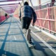 First-time juvenile offenders: Teen skateboarder in jeans and blue plaid shirt speeds through the pedestrian walkway on paved road over red metal bridge