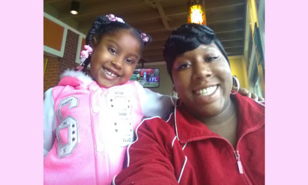 Guaranteed income: Black woman in red sweatshirt with young black girl in pink sweatshirt sit next to each other smiling broadly into camera.