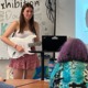 Competency-based innovative high school: Teen girl with long dark hair in white top and red print skirt stands with white guitar in front of classroom singing a song