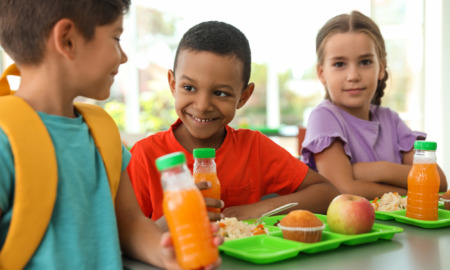 Summer EBT in schools, school meals: Three elementary children sit at table with lime green trays earing lunch