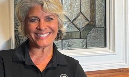 Everyday Heroes: Headshot Andrea Hancock middle-aged woman with short silver hair in black shirt with P.E.S.T. round logo in white, in front of leaded glass window of red brick building