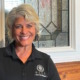 Everyday Heroes: Headshot Andrea Hancock middle-aged woman with short silver hair in black shirt with P.E.S.T. round logo in white, in front of leaded glass window of red brick building