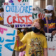 Childcare providers organizing: Protesrers with signs reading "Childcare Crisis" and "Childcare 4 All" gathered together outside on a sunny day