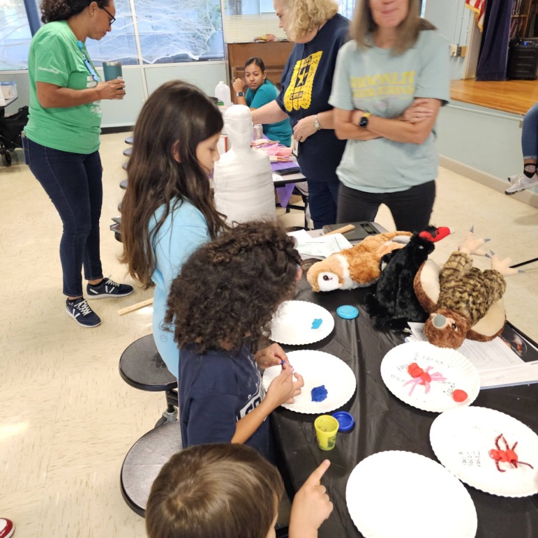 AI afterschool: Several elementary students work at table on project while adults stand in background