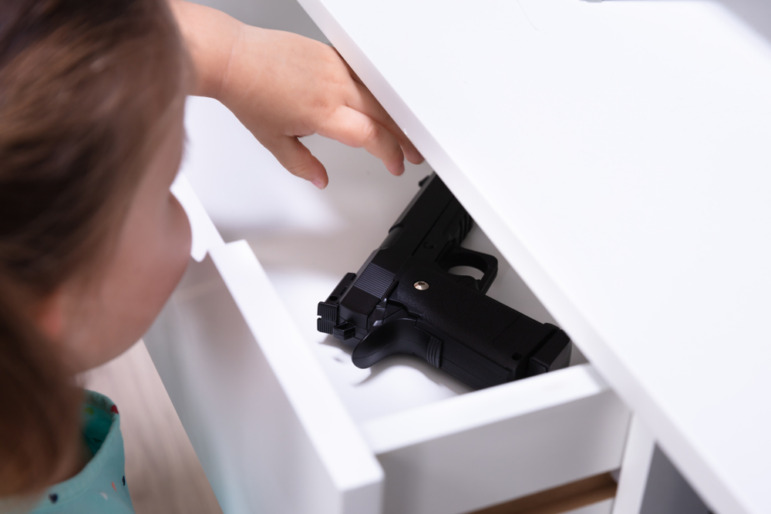 Gun Safety ar Home; Very young girl reaches for hand gun she finds in white drawer