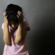 Suspension disabled students: young girl with dark hair in pink r-shirts holds head in hands with angry face against shadowed, dark background