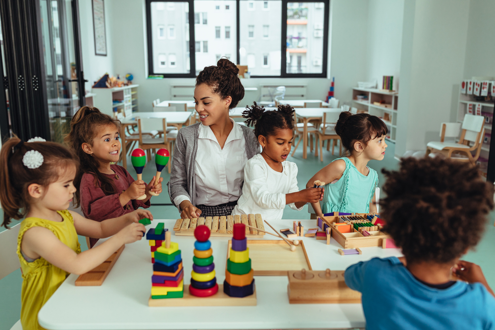 Child care teachers: Mixed ethnic group of preschoolers sit at activity table with female teacher