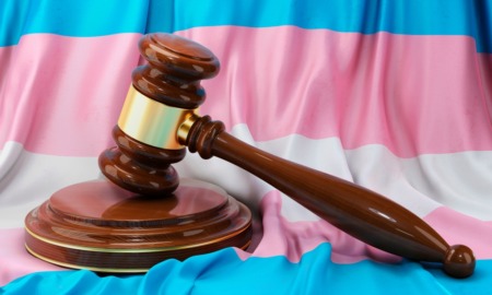 Anti-trans laws, Transgender locker room ruling: Transgender flag with white, pale blue and pale pink stripes sits behind a brown wood courtroom judge's gavel