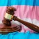 Anti-trans laws, Transgender locker room ruling: Transgender flag with white, pale blue and pale pink stripes sits behind a brown wood courtroom judge's gavel