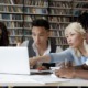 College Essay after affirmative action ended: Four multiethnic schoolmates look at laptop in library discussing information they see on screen